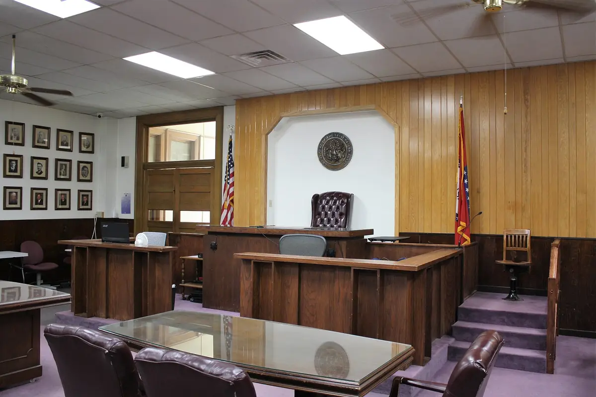 Courtroom front with a wood-paneled judge's bench, witness stand, flags and counsel tables