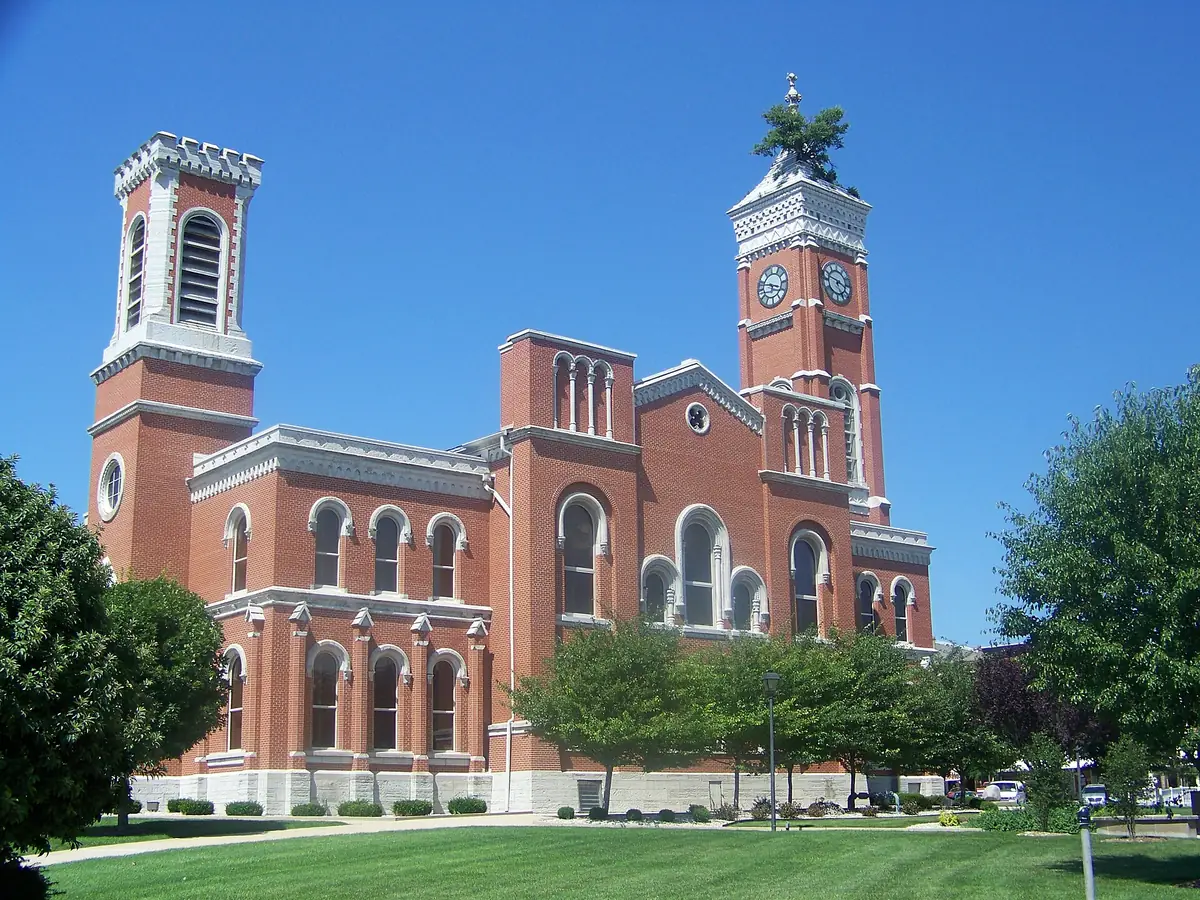 Red brick courthouse with a tall clock tower and a small tree growing from the top of the tower