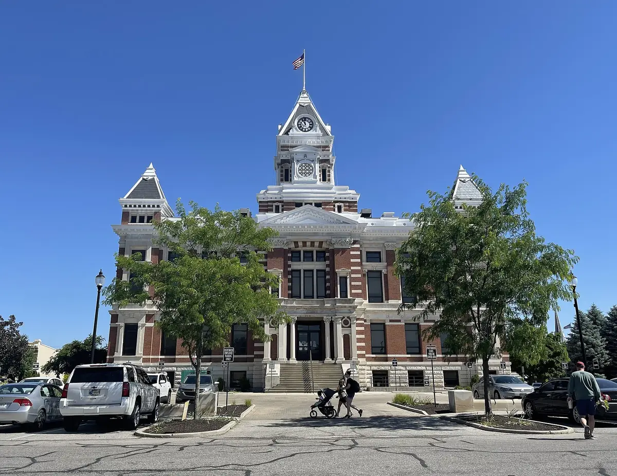 Ornate stone county courthouse with a central clock tower and flags under a clear blue sky