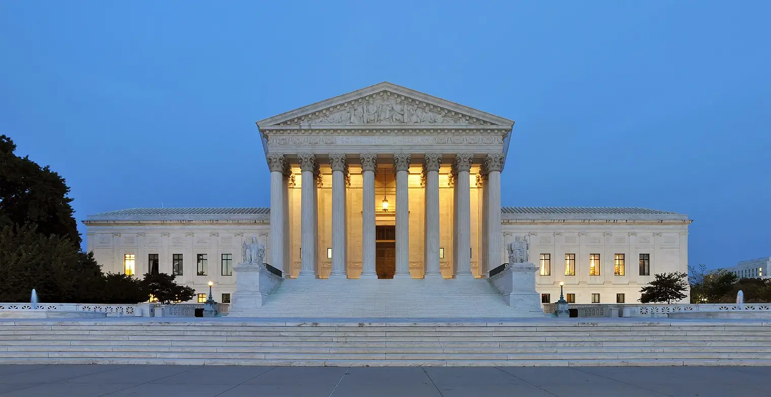 Marble facade of the U.S. Supreme Court Building with lit columns at dusk