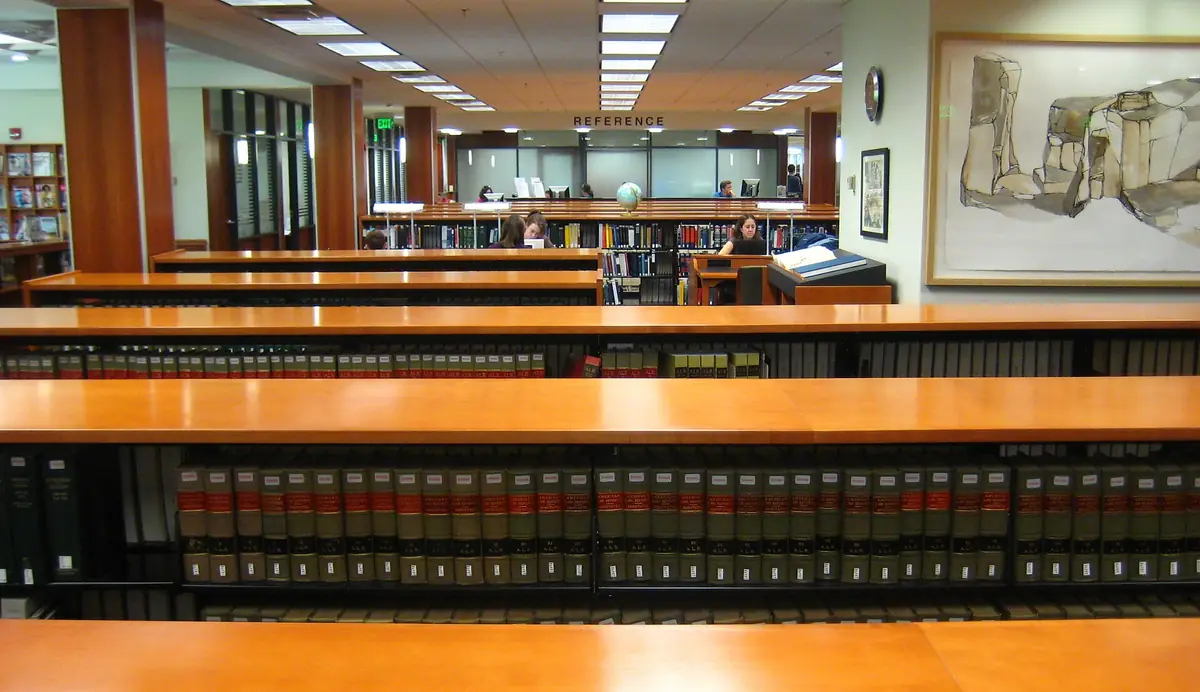 Rows of bound law reporters on low shelves beneath long wooden reading tables in a law library