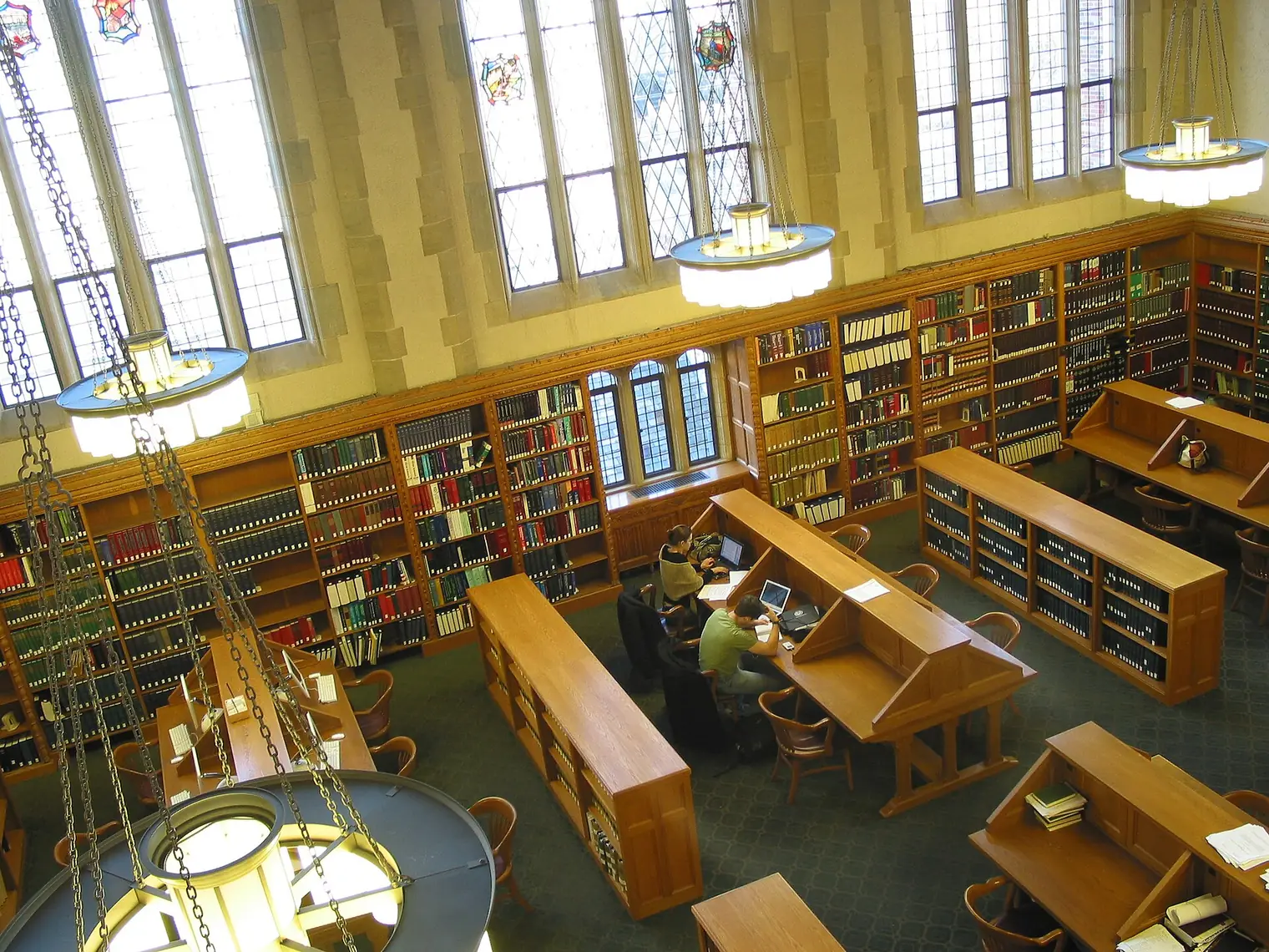 Law library reading room seen from above, with tall leaded windows, wooden bookcases and two people studying at long desks